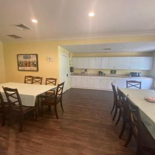 A spacious dining room with multiple tables and chairs, adjacent to a kitchen area.