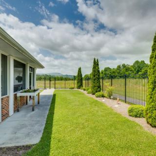 A spacious backyard with a green lawn and a metal fence, surrounded by trees under a partly cloudy sky.