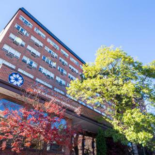 A hospital building with a brick exterior, surrounded by trees under a clear blue sky.