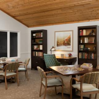 A cozy library room with wooden bookshelves, tables, and chairs under a wooden ceiling.