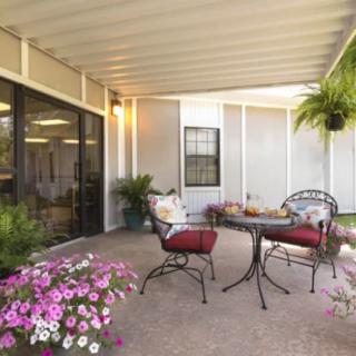 A cozy patio with a table and two chairs, surrounded by flowers and plants.