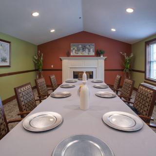 A dining room with a long table set for a meal, featuring plates and chairs, and a fireplace in the background.