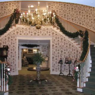 A beautifully decorated grand staircase adorned with Christmas garlands and a chandelier, exuding traditional holiday charm.