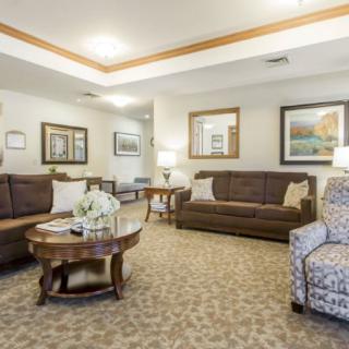 A cozy living room with two sofas, a patterned armchair, and a wooden coffee table, adorned with framed artwork and soft lighting.