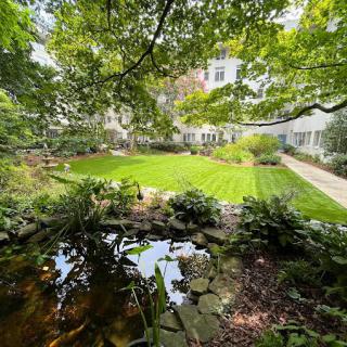 A serene garden view with a small pond and lush green lawn surrounded by trees.