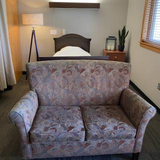 A cozy living space featuring a patterned sofa, a single bed, a lamp, and a small plant.