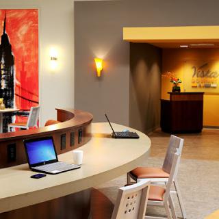A modern lobby area with a reception desk, artwork on the wall, and workstations for guests.