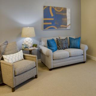 A cozy living room with a sofa and armchair, decorated with cushions and a modern lamp.
