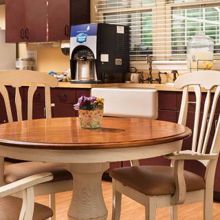 A cozy kitchen with a round dining table and chairs, featuring a coffee maker on the counter.