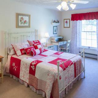 A cozy bedroom with a red and white quilted bed, desk, and large window.