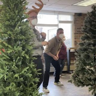 A lively indoor scene with people playfully interacting amidst Christmas tree decorations.