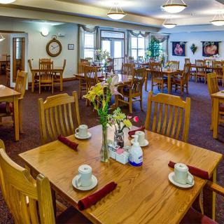 A cozy and elegantly decorated dining room with wooden tables and chairs, featuring a well-arranged table setting with flowers as a centerpiece.