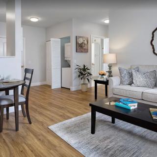 A modern living room interior featuring a cozy sofa, coffee table, and dining area with wood flooring.