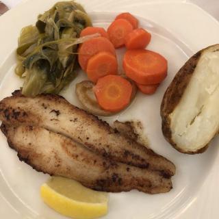 A plate of grilled fish served with carrots, cabbage, a baked potato, and a lemon wedge.