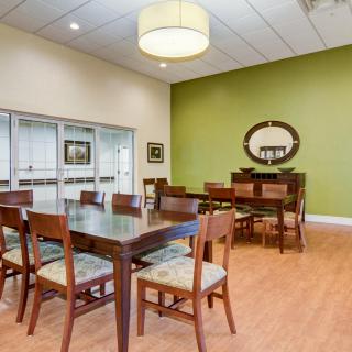 A well-furnished dining room with a large table, chairs, and a mirror on the green accent wall.