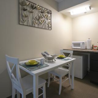 A minimalist dining area with a white table and chairs, set for two, next to a kitchenette.