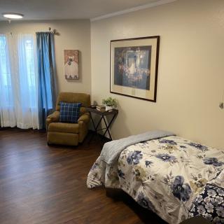 A cozy bedroom with a floral-patterned bed, an armchair, and artwork on the wall.