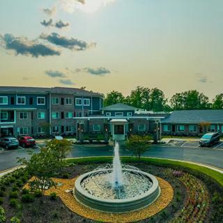 A scenic view of a building with a central fountain surrounded by parked cars and landscaped greenery.