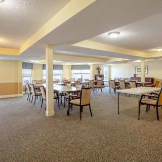 A spacious dining room with multiple tables and chairs, featuring carpeted flooring and ample lighting.