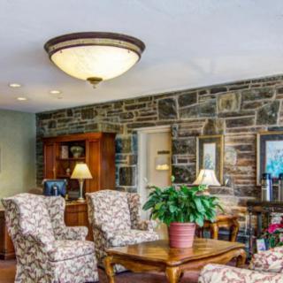 A cozy living room with patterned chairs, a wooden table, and a stone accent wall.