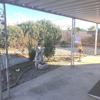 A backyard patio with a shade structure, featuring a garden area and a decorative statue.