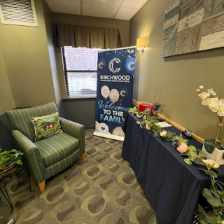 A cozy waiting area featuring a green chair, decorative table with flowers, and an informative banner.