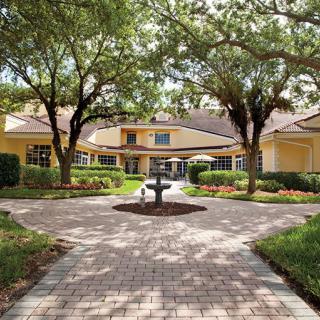 A landscaped courtyard with a fountain and pathway leading to a building surrounded by trees.