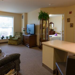 A cozy living space with a view into the adjacent bedroom, featuring comfortable furniture and decorative plants.