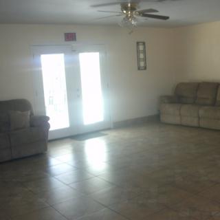 A spacious living room with two sofas, a ceiling fan, and tiled flooring, illuminated by natural light from French doors.