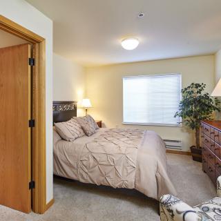 A cozy bedroom with a neatly arranged bed, decorative lamps, and a potted plant by the window.