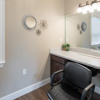 A stylish vanity area with a mirror, chair, and decorative wall elements.