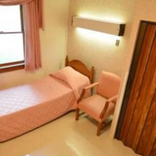 A simple bedroom with a single bed, pink bedding, and a chair by the window.