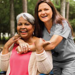 A nurse happily embracing an elderly woman in a wheelchair while outdoors.