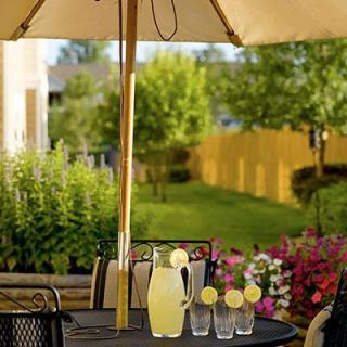 A sunny patio setting with a table featuring a pitcher of lemonade and glasses under an umbrella.