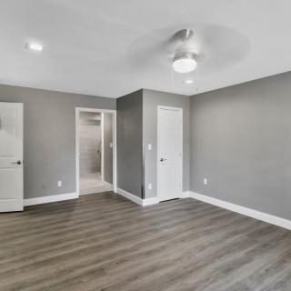 A modern empty room with gray walls and hardwood flooring, featuring a ceiling fan and recessed lighting.