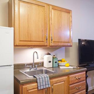 A cozy kitchen with wooden cabinets, a sink, and a countertop next to a refrigerator and television.