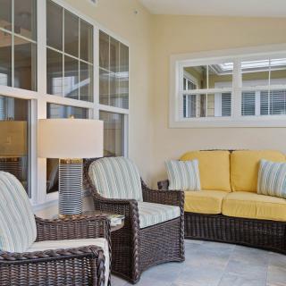 A cozy sunroom with wicker furniture and bright yellow cushions, complemented by a stylish lamp.