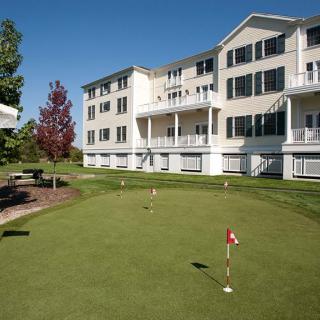 A scenic view of a putting green in front of a multi-story apartment building on a sunny day.