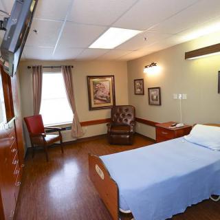 A well-lit hospital room featuring a single bed, a comfortable chair, and framed artwork.
