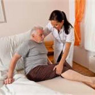 A nurse assisting an elderly man on a bed in a healthcare setting.