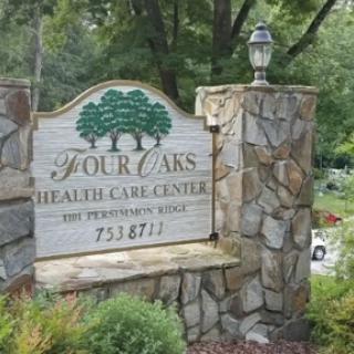 Entrance sign of Four Oaks Health Care Center, featuring stonework and surrounded by greenery.
