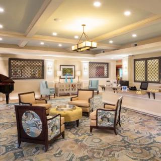 A spacious and elegantly decorated living room featuring a seating area with plush chairs, a decorative carpet, and ambient lighting.