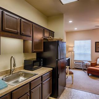 A cozy apartment interior featuring a compact kitchen area with dark wooden cabinets, leading into a warmly lit living room.