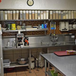 An industrial kitchen setup with shelves of ingredients and a sink area.