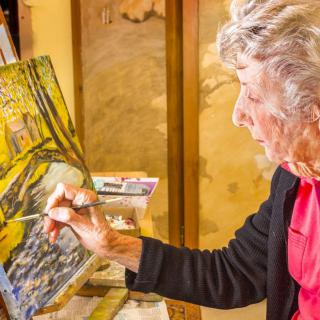 An artist focuses intently as she paints on a canvas indoors.