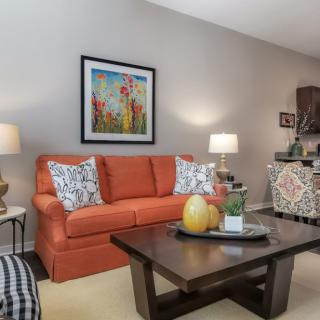 A cozy living room with an orange sofa, colorful artwork, and a wooden coffee table adorned with decorative items.