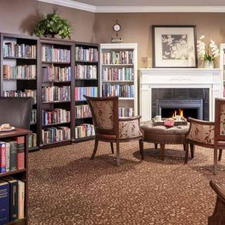 A cozy library with bookshelves, a fireplace, and comfortable armchairs.