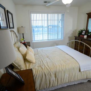 A cozy bedroom with a neatly made bed, dresser, and a large window letting in natural light.
