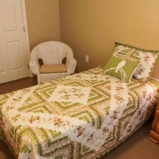 A cozy bedroom with a single bed adorned with a patterned quilt and a wicker chair in the corner.