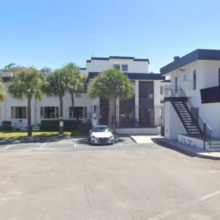 Modern apartment complex with palm trees and a parking lot on a sunny day.